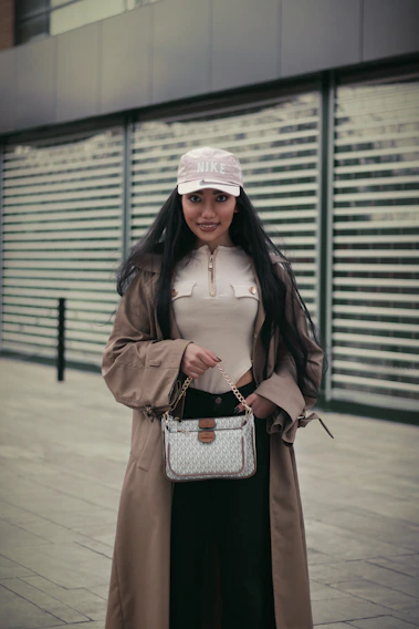 A chic street style shot featuring a model in a flowing trench coat and bold accessories against an urban backdrop.