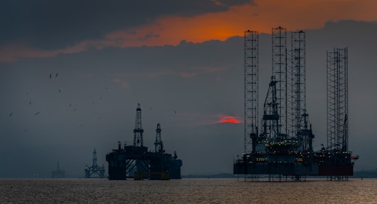 A panoramic view of a bustling Richgates Holdings construction site blending with offshore oil rigs at sunset.