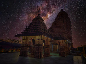 A serene Bhutanese temple silhouetted against a vast star-filled midnight blue sky.