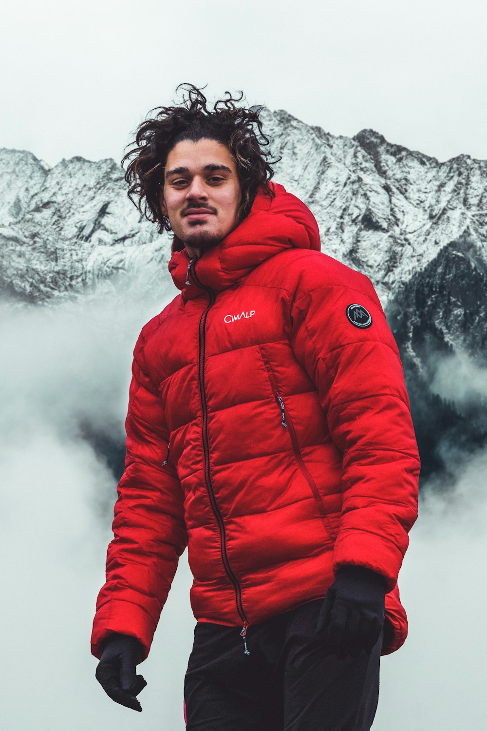a man wearing a red coat and standing in front of a mountain