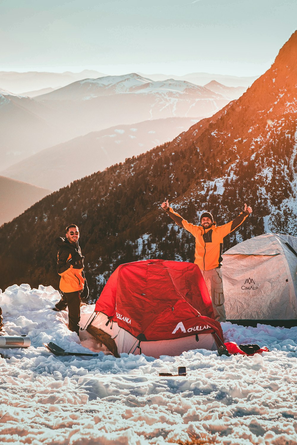 a group of people stand around a tent in the snow