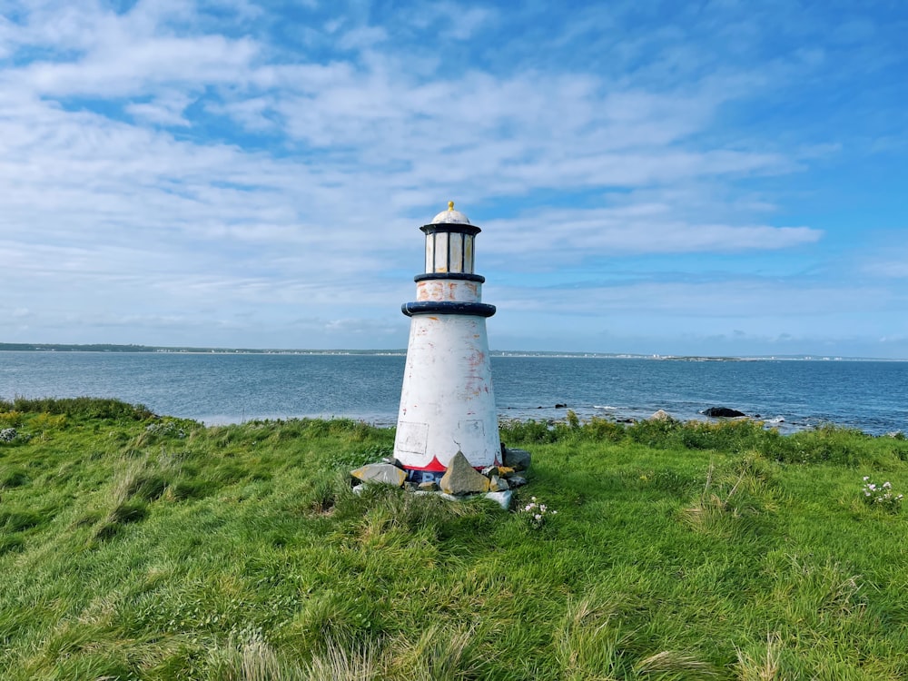 a lighthouse on a grassy hill by the water
