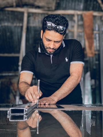 Close-up of a craftsman inspecting a large mirror with precision tools in a bright workshop.