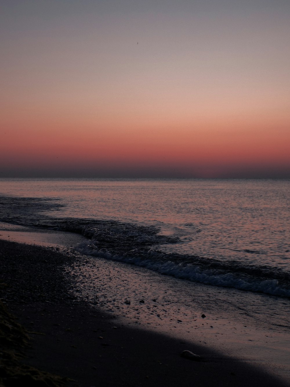 a beach with waves and a pink and purple sky