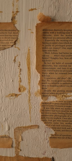 The image features a close-up of weathered, yellowed paper fragments adhered to a rough, textured wooden surface. The text on the paper is partially legible, with references to personal anecdotes. There are noticeable marks and stains on both the paper and the wood, contributing to an aged and rustic appearance.