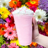 a hand holding a plastic cup with a pink substance in it