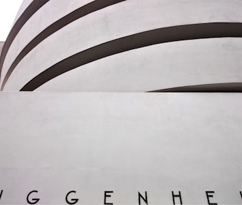 Curved architectural lines form the top of a modern building facade. The letters 'GGENHEI' are partially visible at the bottom.