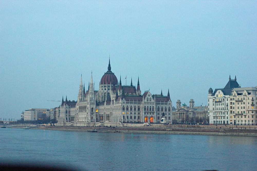 um corpo de água com edifícios ao longo dele com o edifício do Parlamento húngaro ao fundo