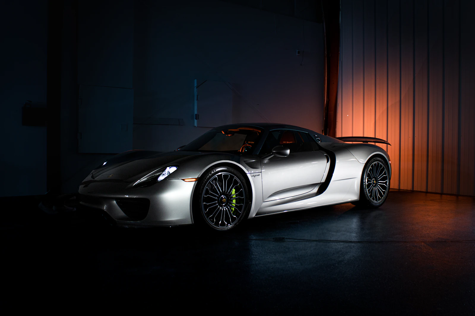 Silver Porsche 918 Spyder in a dark room with warm lighting