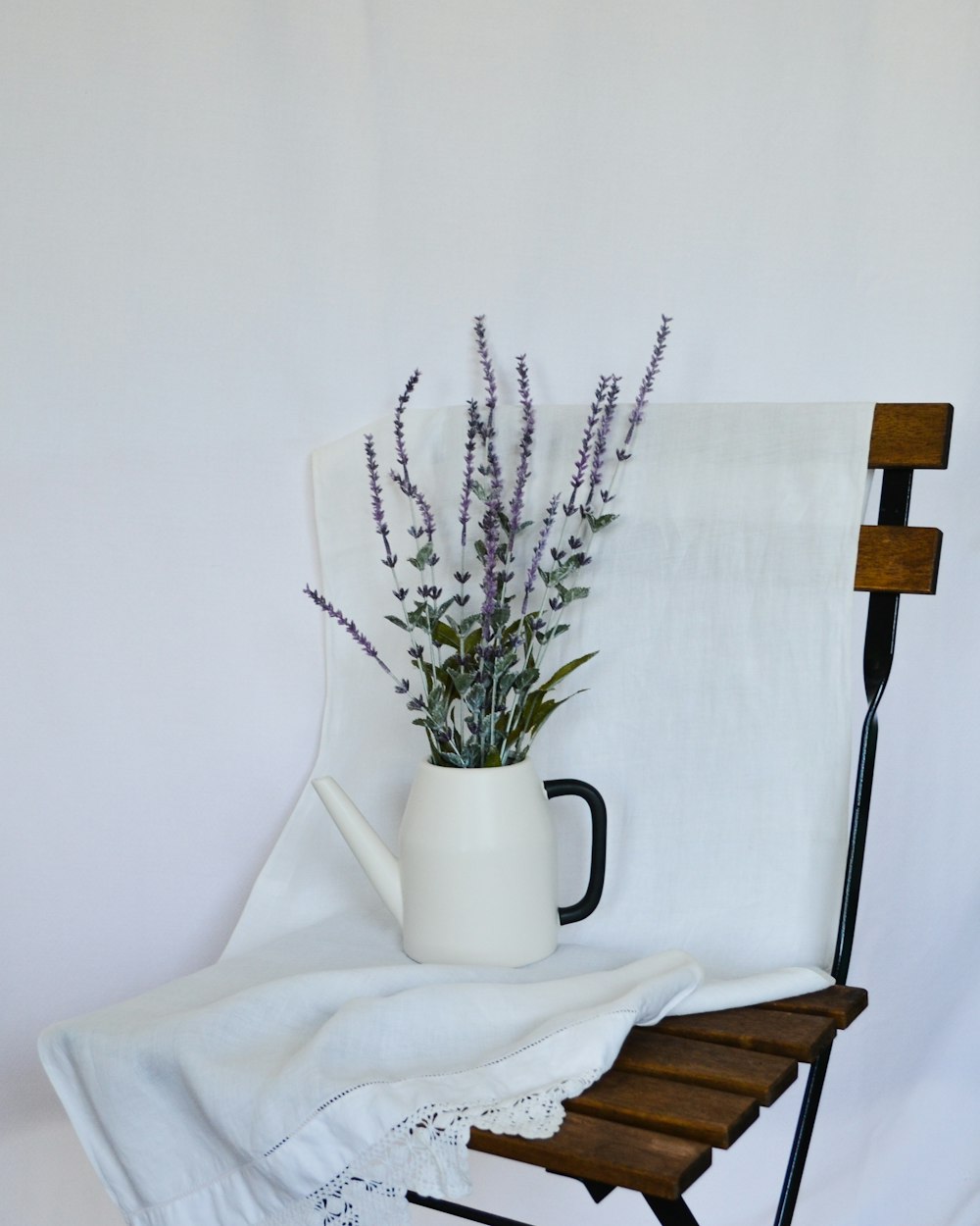 a vase with purple flowers on a white bed