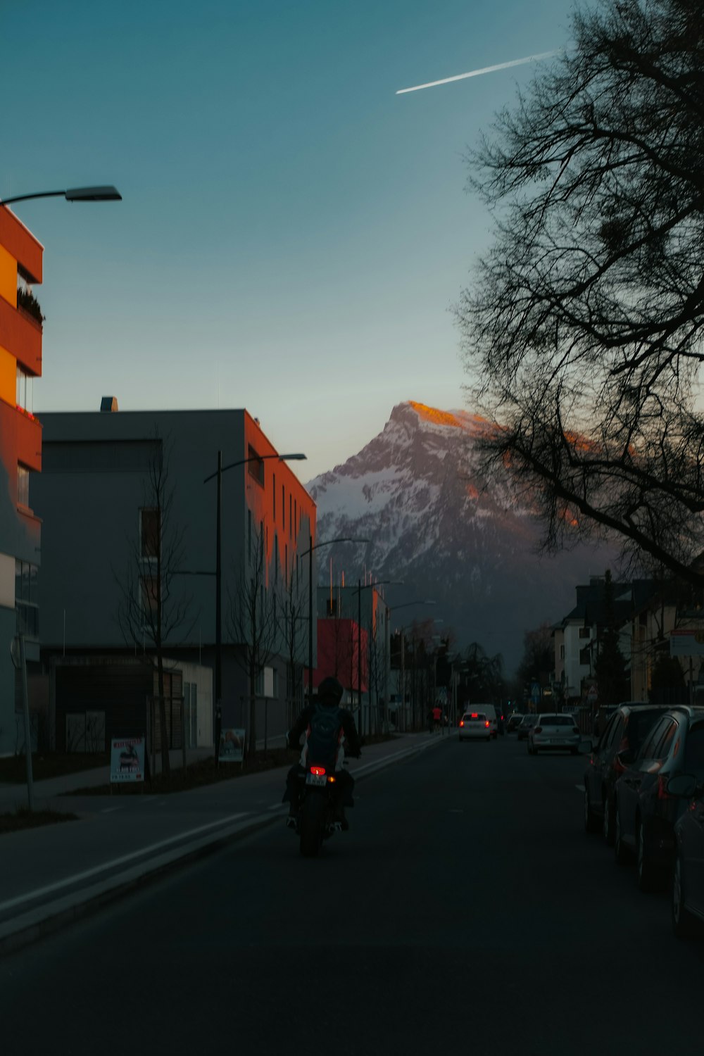 uma pessoa que monta uma motocicleta em uma rua com edifícios e uma montanha ao fundo