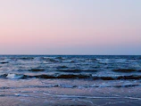A peaceful morning view of the shoreline where the sea meets the sky, with gentle waves lapping the sand.