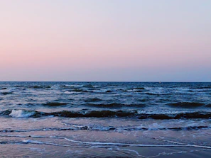 A peaceful morning view of the shoreline where the sea meets the sky, with gentle waves lapping the sand.