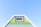 A brightly painted triangular house facade features pastel blue, green, and yellow horizontal stripes. It includes a small rectangular window with a white frame near the top. The facade is set against a clear blue sky, creating a fresh and vibrant appearance.