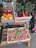 A display of fresh produce at a market with boxes filled with colorful fruits and vegetables. There are golden and red apples, vibrant red and green rainbow chard, and bunches of bright red breakfast radishes with green leaves. Each type of produce is labeled with small slate signs showing their names and prices.