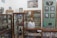 An old pharmacy with wooden display cabinets filled with various bottles and containers. A mannequin wearing a white lab coat stands behind the counter. Several framed photographs and vintage advertisements adorn the walls. The atmosphere invokes a sense of nostalgia and history.
