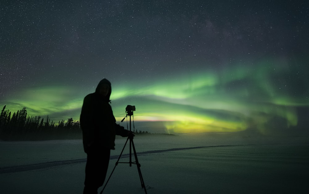 a person standing on a snowy field with a camera and a bright light in the sky