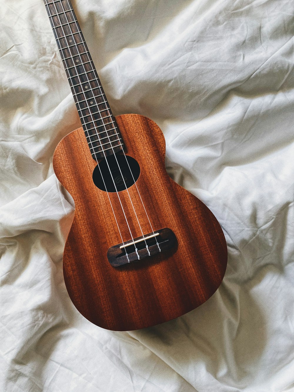 Una guitarra marrón sobre una sábana blanca