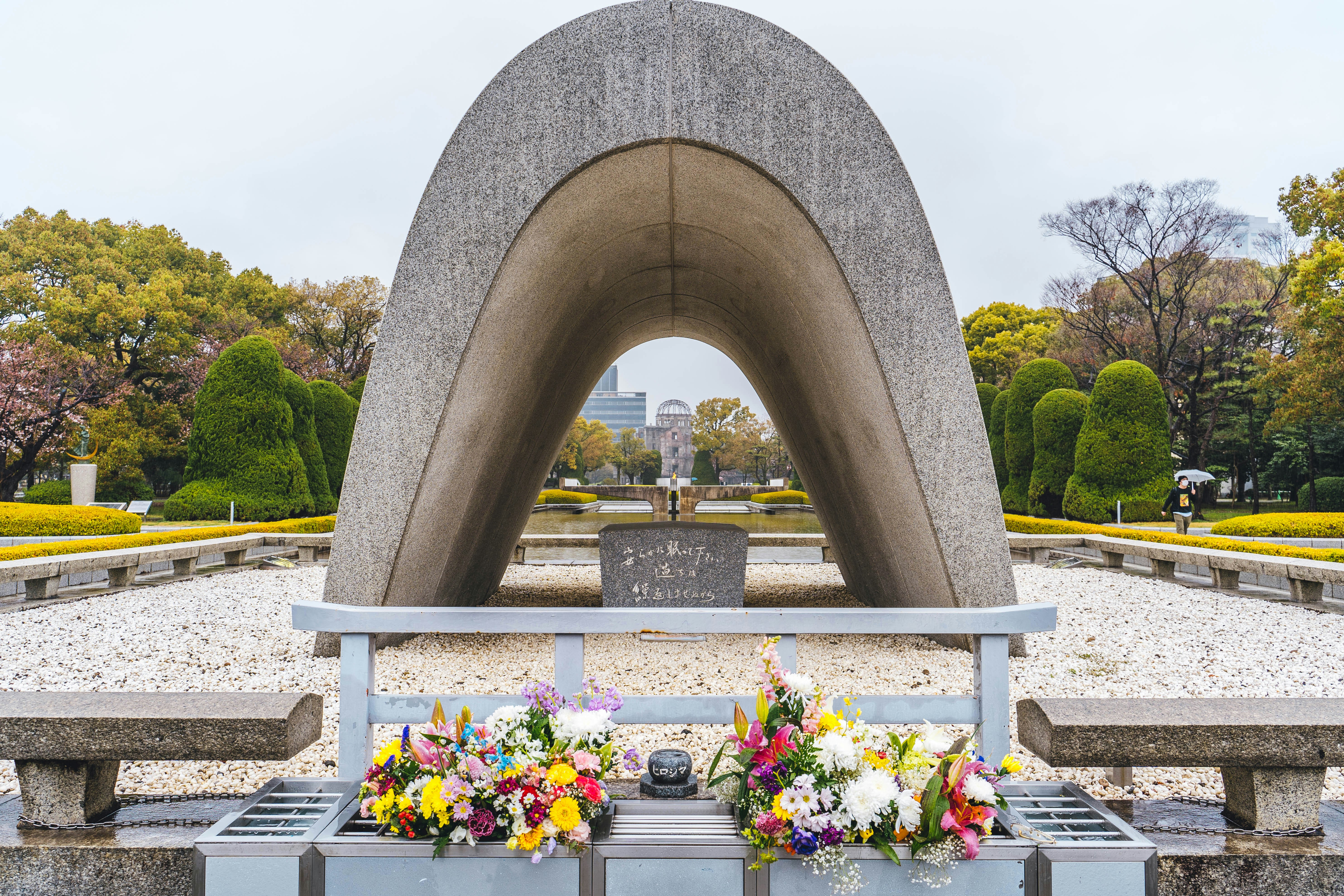 a large stone structure with flowers in front of it with Hiroshima Peace Memorial in the background