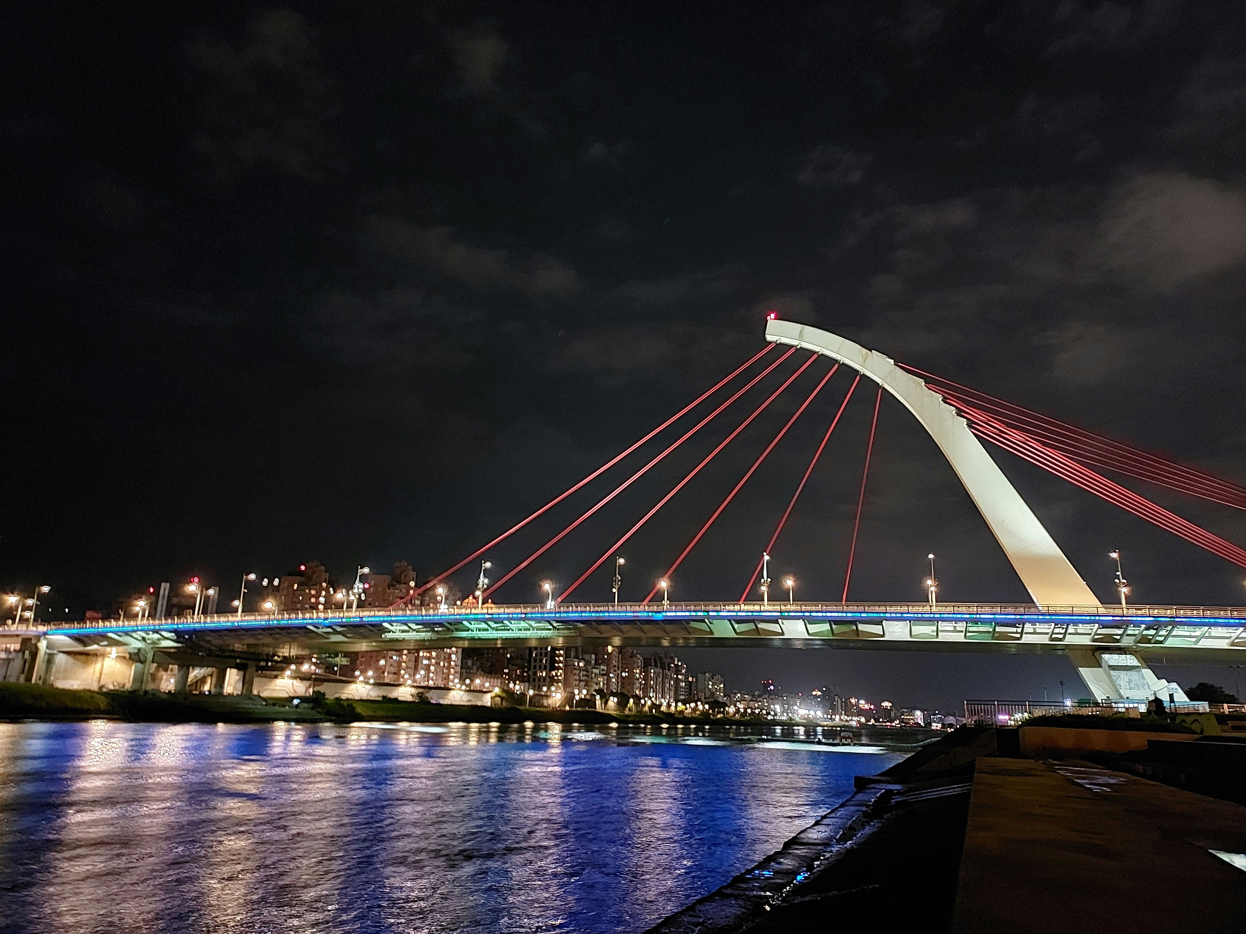 Modern bridge with steel and aluminum cables at night with dark sky and city lights in background