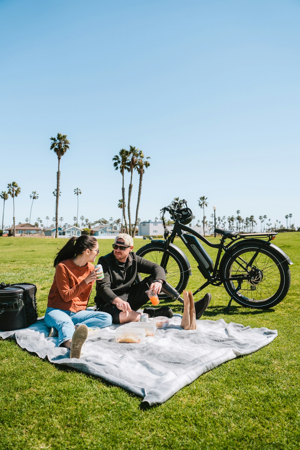 a man and woman sitting on a blanket in a grassy area