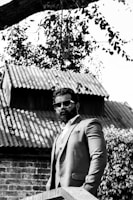 A rugged man with a wild beard standing confidently on a city rooftop at dusk.