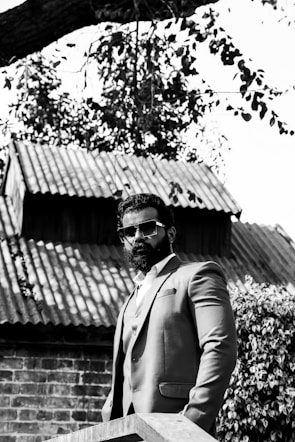 A rugged man with a wild beard standing confidently on a city rooftop at dusk.