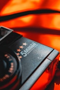 A close-up of a camera featuring the words '5 Million' with stars above it, against a vibrant orange background. The focus is on the brand text and stars, with a contrasting and warm color scheme adding emphasis.