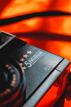 A close-up of a camera featuring the words '5 Million' with stars above it, against a vibrant orange background. The focus is on the brand text and stars, with a contrasting and warm color scheme adding emphasis.