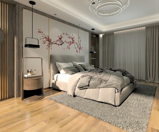 A modern bedroom features a large bed with grey bedding and pillows, flanked by two nightstands with black pendant lights hanging above them. A textured area rug covers the wooden floor, and the wall behind the bed has paneling with artistic floral designs in shades of pink and red. Full-length curtains cover the window, and a contemporary ceiling light fixture adds elegance to the room.