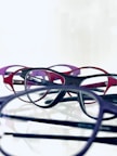A flat lay of various colorful eyeglass frames and a pair of contact lenses on a clean white surface.