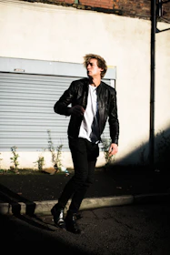 A dynamic shot of a model walking down a city street wearing a black leather jacket and beige trousers, capturing movement and urban energy.