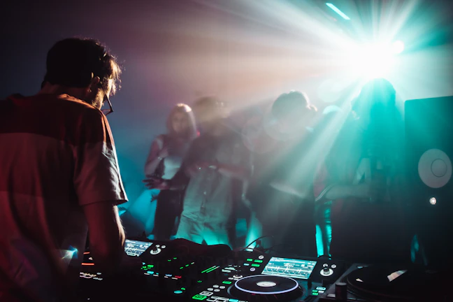 A vibrant DJ mixing music with a joyful crowd dancing under warm yellow and red lights.