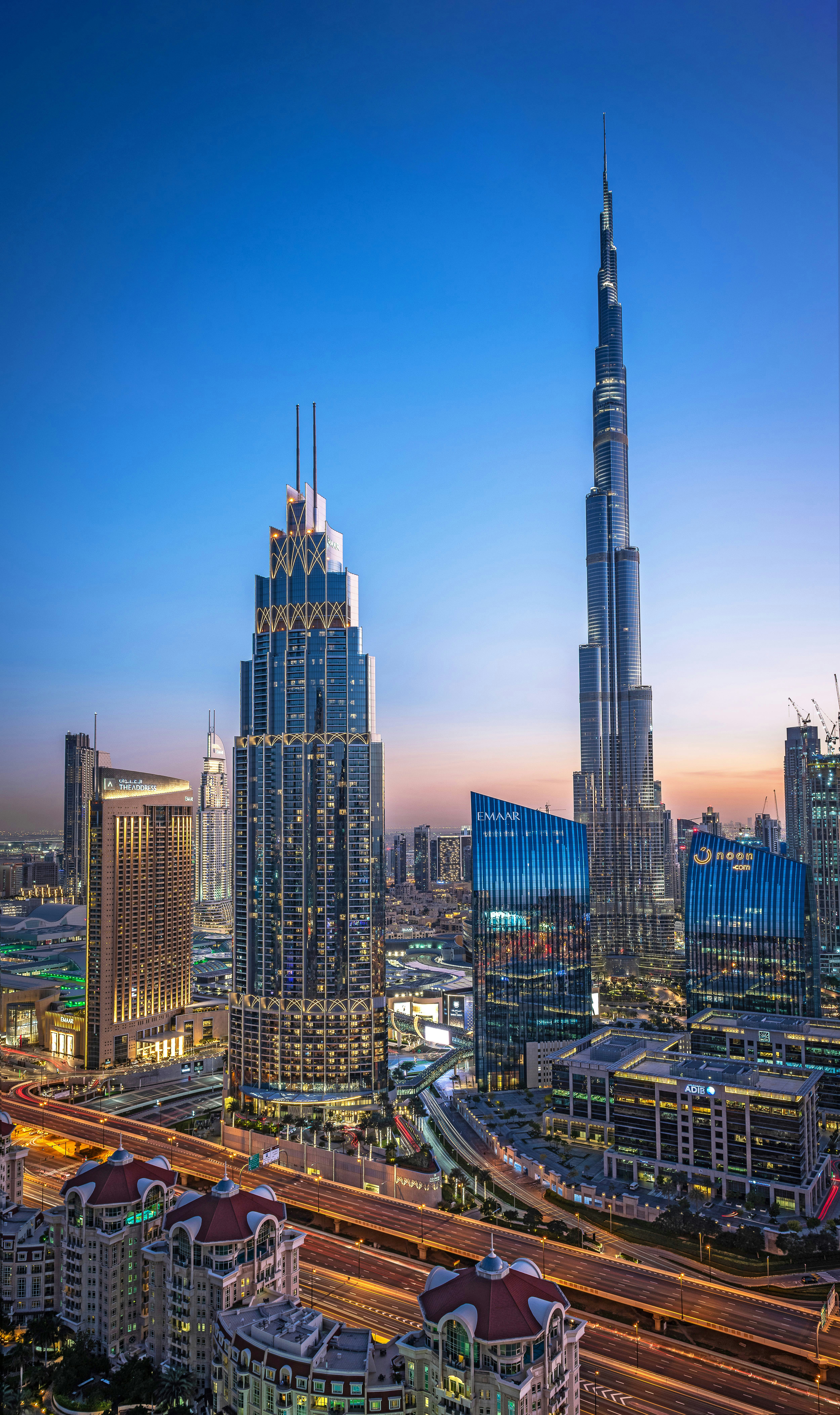 Dubai skyscrapers at deep blue twilight, illuminated towers against dark indigo sky, moody atmospheric haze