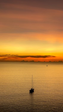 A serene sunset over a calm ocean with a luxury yacht sailing gently, reflecting warm orange hues.