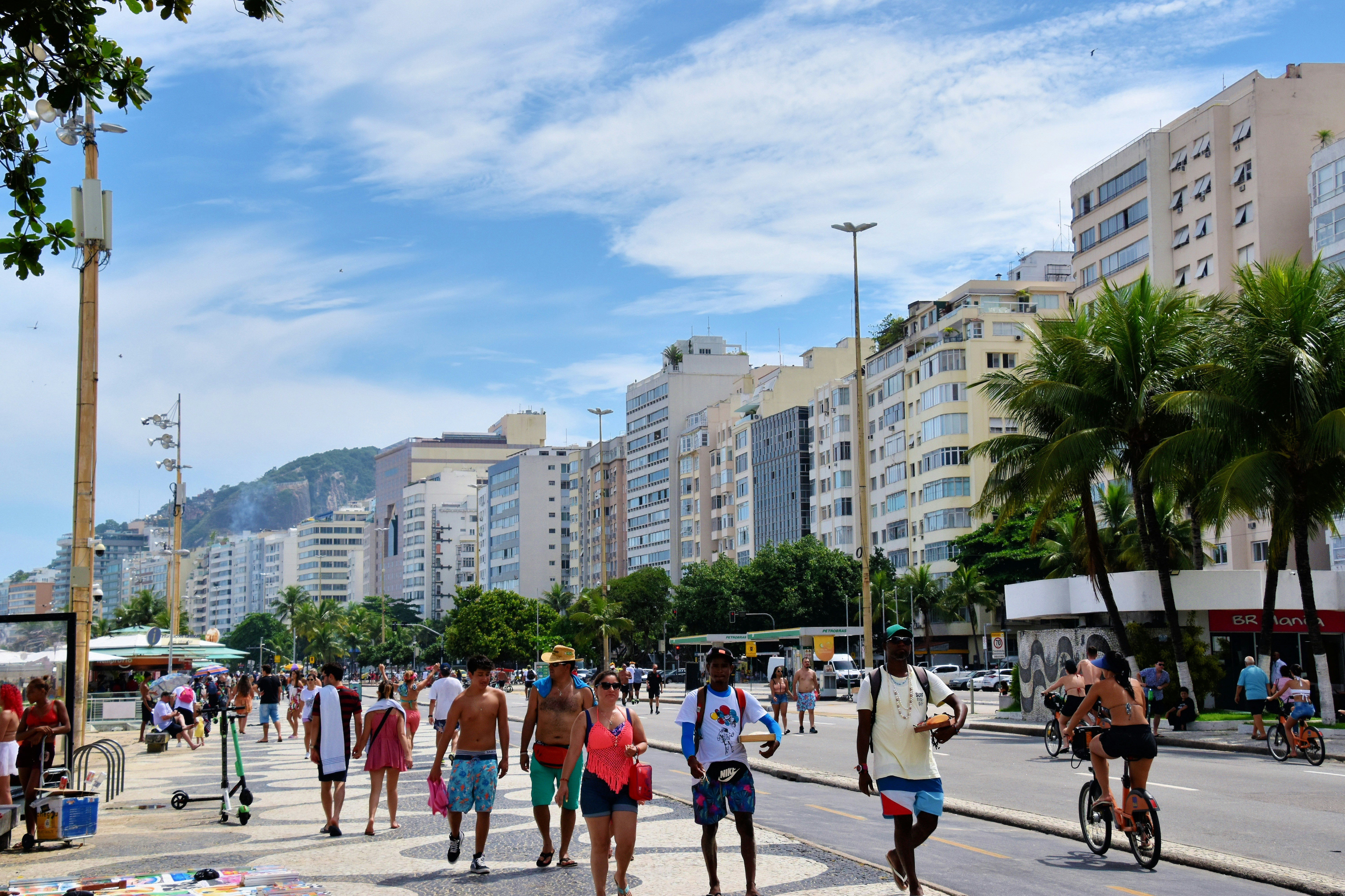 a group of people walking on a street with palm trees and buildings in the background