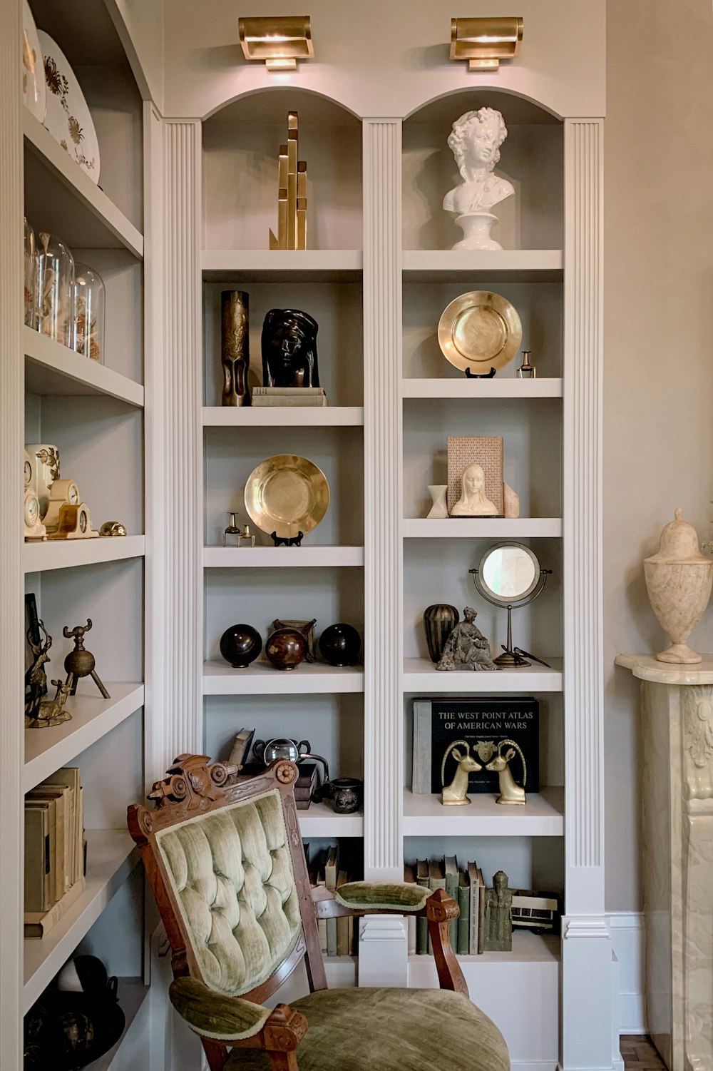 a white shelving unit with chinaware and a chair