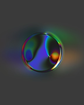 A reflective bubble-like object with an iridescent surface displaying a spectrum of colors, including shades of green, blue, and purple, against a dark gray background.