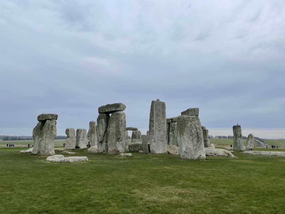 a group of rocks in a grassy field with Stonehenge in the background