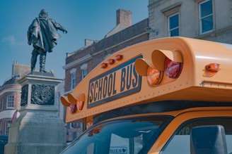 A bright yellow school bus parked in front of a school building with happy children boarding.