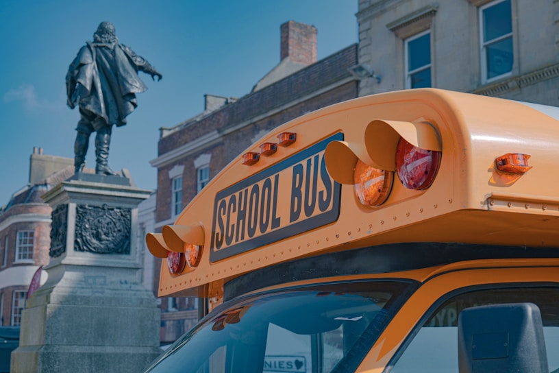 A bright yellow 74-seater school coach parked outside a historic museum on a sunny day.