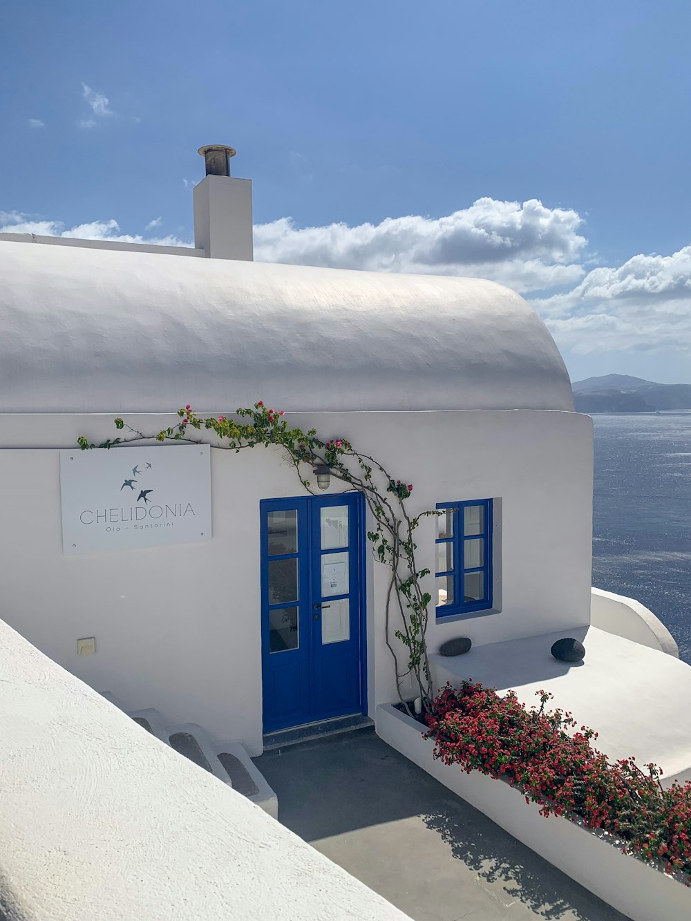 a white building with blue doors and a white wall with a tower and a white building with a