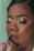A person is having their makeup done, focusing on their face with eyes closed. They have glittery eye makeup and long eyelashes. A hand is applying lip liner to the lips, indicating a makeup session.