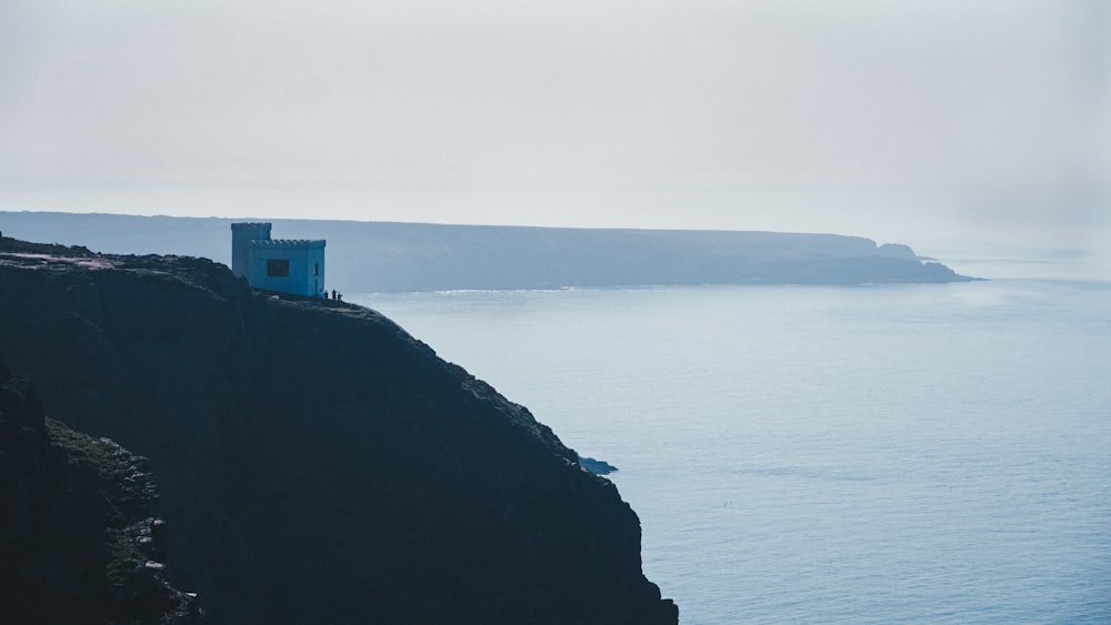 a blue building on a cliff above the ocean
