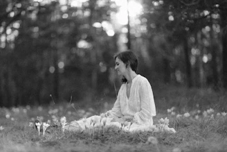 A serene woman sitting peacefully in nature, surrounded by soft sunlight and blooming flowers.