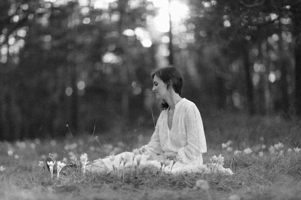 A serene woman sitting peacefully in nature, surrounded by soft sunlight and blooming flowers.