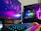 A gaming setup featuring a desktop computer tower with colorful RGB lighting, a Philips monitor displaying a vivid abstract design, a mechanical keyboard with RGB backlighting, and a pair of nearby speakers. The computer tower showcases components like an MSI GeForce RTX graphics card and NZXT cooler.