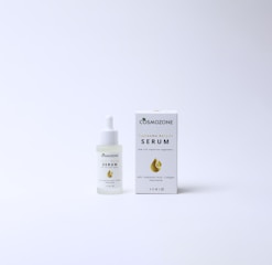 A bottle of Cosmozone serum with a dropper cap is placed next to its packaging box. The box features a golden droplet design, a green leaf icon, and text indicating anti-aging properties and ingredients such as hyaluronic acid, collagen, and niacinamide. Both items are on a plain, light background.