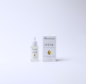 A bottle of Cosmozone serum with a dropper cap is placed next to its packaging box. The box features a golden droplet design, a green leaf icon, and text indicating anti-aging properties and ingredients such as hyaluronic acid, collagen, and niacinamide. Both items are on a plain, light background.