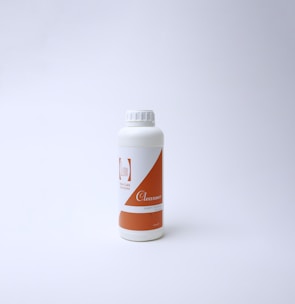 A white plastic bottle with an orange label on a plain white background. The label features text including the word 'Cleanser' and a logo with minimalistic design. The bottle has a screw cap and is positioned slightly to the left of the center.